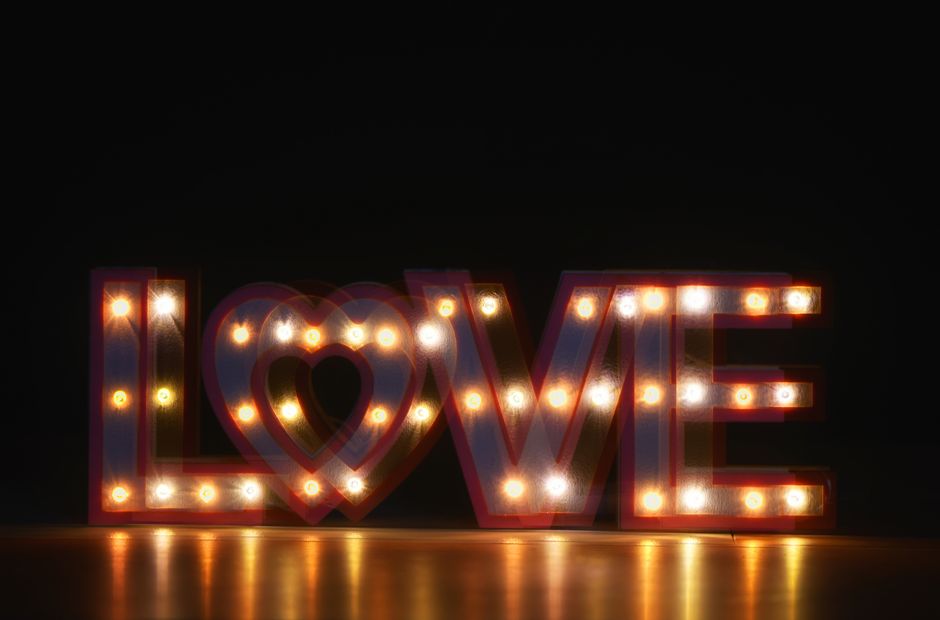 A close-up of an illuminated 'LOVE' sign with warm glowing lights against a dark background.